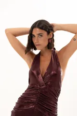 Vestido largo de fiesta en tejido brillante color bordó, con escote halter profundo, detalle de frunces en la cintura y tajo lateral en la falda.