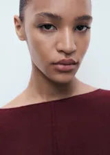 Jersey de punto fino con diseño oversize, cuello barco y mangas acampanadas. Presenta un corte cropped y costura central vertical en el frente.