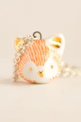 Collar con dije de zorro blanco con detalles en naranja y dorado, y cadena plateada.