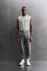 Pantalón jogger gris de corte regular fit, confeccionado en tejido de algodón con interior afelpado. Cuenta con cintura elástica ajustable con cordón, bolsillos laterales de vivo y traseros de plastrón. Presenta un texto estampado en color bordó en la pernera y bajo acabado en puño con elástico. Incluye un parche con logo combinado a contraste en la cintura.