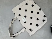Tote bag de algodón color negro con estampado de lunares blancos. Cuenta con doble asa de hombro y etiqueta frontal con el logo de la marca.