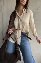 Camisa beige de tejido liviano y calce relajado, con manga larga y detalle de puntilla y bordado en contraste que recorre el frente.