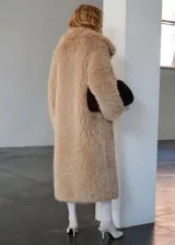 Campera larga de abrigo con textura peluda tipo corderito sintético, en color tostado, con solapas anchas y mangas largas.