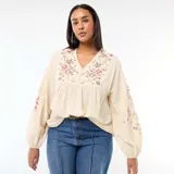 Blusa de color beige con cuello en V, mangas largas abullonadas con puños elásticos y bordados florales en el pecho y las mangas.