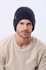 Gorro de punto grueso con diseño acanalado y doblez en el borde. Incluye una pequeña etiqueta decorativa de cuero sintético en el lateral.