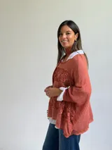 Sweater de punto color naranja con diseño holgado, que incorpora franjas horizontales de encaje con motivos florales. Presenta mangas tres cuartos con puños abotonados y se complementa con una bufanda del mismo tejido y color.
