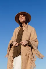 Poncho beige de tejido de punto con flecos y cuello alto.