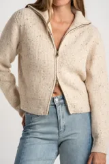 Cardigan de punto acanalado en color beige melange con motas oscuras. Presenta un diseño ajustado al cuerpo, cierre frontal completo con cremallera metálica y cuello alto.
