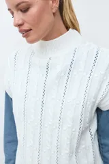 Chaleco de tejido de punto color crudo, con diseño de ochos verticales y cuello redondo. Presenta un corte holgado y terminaciones acanaladas en cuello, sisas y ruedo.