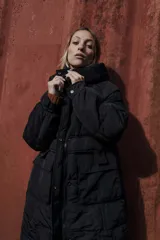 Campera larga acolchonada color marrón, con diseño midi, capucha amplia, cierre frontal con cremallera y broches, y bolsillos delanteros con tapa.