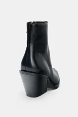 Botín estilo cowboy de caña baja, confeccionado en material sintético con acabado liso. Presenta un diseño de punta fina, tacón curvo en bloque y cierre mediante cremallera lateral.