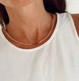 Collar tipo gargantilla elaborado con cuentas de cristal en tono rosa pálido, intercaladas con cuentas en tonos oscuros y detalles metálicos dorados. Cuenta con cadena extensora.