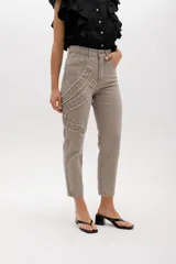 Jean estilo mom fit en tono gris lavado, con tiro alto y cierre frontal. Presenta un aplique fruncido en forma de espiral en la pierna izquierda con bordes deshilachados, bolsillos funcionales y corte recto al tobillo.