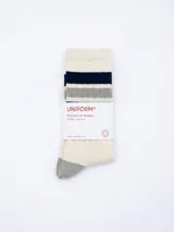 Medias de caña media en color crema, con diseño de rayas horizontales en azul marino y gris en la parte superior. Presentan puntera y talón en color gris, con la palabra 'UNIFORM' bordada en azul claro en el lateral.
