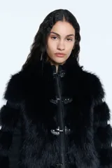 Campera de pelo ecológico negro con recortes en denim negro. Presenta cierre metálico frontal, alamares metálicos decorativos, capucha y bolsillos laterales. Las mangas tienen un diseño con recortes que alternan pelo y denim, y cuenta con elástico en la cintura.