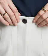 Pantalón zanahoria de sastrería color blanco, con cintura alta, trabillas y botón contrastante.