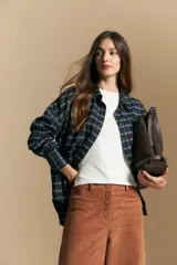 Camisa de estilo leñador con estampado de cuadros en tonos azul, negro y marrón. Presenta cuello clásico, cierre frontal con botones y mangas largas con puños abotonados.