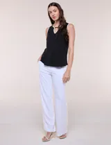 Blusa sin mangas de seda fría marca Rio & Rian, color blanco con ribetes negros en cuello y sisas. Presenta un escote redondo con abertura tipo gota en el frente y un aplique metálico decorativo.