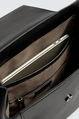 Mochila negra de poliuretano, con solapa y cierre de hebilla. Tiene un compartimento principal con espacio para dispositivos electrónicos de hasta 13 pulgadas y un bolsillo con cierre. En la parte frontal tiene un bolsillo con cierre y bolsillos planos en la parte frontal y posterior. Tiene asa de mano y dos asas de hombro ajustables y acolchadas.