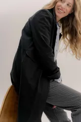 Tapado largo de jean azul oscuro, con cuello solapa y puños con detalle de cinta de terciopelo negro. Presenta costuras visibles que definen paneles y un logo bordado en la espalda.