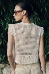 Top de cuello redondo y mangas sisa con volantes, confeccionado en tejido de punto calado con algodón y bajo con detalle de volantes.