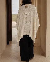 Ruana de algodón color beige, de textura suave y caída envolvente, con detalle de bordado en la espalda y aplique de cuero en el cuello.