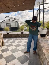 Sweater verde tejido con cuello redondo y diseño de cabeza de vaca en cuero marrón con bordados a mano en color beige.