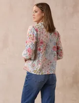 Blusa de gasa plisada con estampado floral en tonos rosas y celestes. Presenta cuello a la base con escote en V y lazo de ajuste frontal, mangas largas con puños elásticos y corte recto.