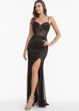 Vestido largo de fiesta color negro, con escote corazón y cuerpo tipo corset con transparencias y detalles brillantes. Presenta breteles finos, falda con tajo lateral profundo y tejido de red con acabado brillante.