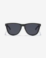 Lentes de sol unisex Hawkers modelo One Raw Carbono, con montura cuadrada negra con textura de fibra de carbono y lentes polarizadas oscuras.