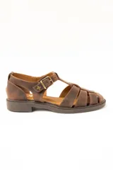 Sandalias tipo cangrejera de cuero color marrón, con diseño de tiras cruzadas, talón cerrado y tira ajustable con hebilla metálica y detalle de estrella grabada en el lateral. Suela plana con pequeño tacón.