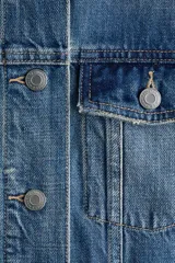 Campera de denim de algodón rígido, color azul, con cuello clásico y cierre frontal de botones metálicos. Cuenta con bolsillos superiores con solapa y botón, bolsillos laterales insertados y puños abotonados.