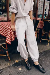 Pantalón jogger de felpa color gris claro melange, de tiro medio con cintura elástica. Presenta detalles de aplicaciones tejidas a contraste en los laterales y terminaciones con puños abullonados.