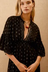 Vestido midi negro con lunares dorados, escote en V, mangas anchas al codo con bordado de lentejuelas y mostacillas. Corte amplio con ajuste elástico en la cintura y forro de algodón.