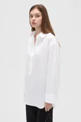 Camisa blanca de algodón, de corte holgado, manga larga con puños anchos y cuello camisero. Cuenta con cierre frontal parcial de botones.