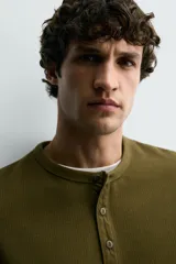 Camiseta de manga corta con cuello panadero y cierre frontal de tres botones. Presenta una textura acanalada y un corte regular fit.