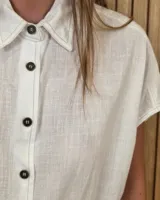 Camisa de manga corta color beige, de corte holgado, con cuello camisero y cierre frontal de botones.