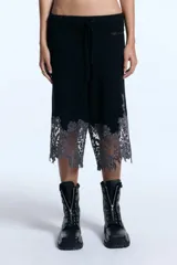 Bermuda de punto en mezcla de lana y alpaca, color negro, de tiro medio y largo hasta la rodilla. Presenta cintura elástica con cordón ajustable y un delicado detalle de encaje gris en el ruedo con diseño irregular.