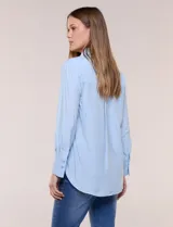 Camisa de calce relajado color celeste, confeccionada en tejido de textura suave y fluida. Presenta cuello camisero y abotonadura frontal, mangas largas con puño ancho y ruedo curvo.