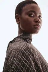 Blusa de manga larga con estampado a cuadros en tonos oscuros (negro/marrón y blanco). Presenta cuello drapeado con tira para atar en la nuca, hombros caídos y cintura entallada con pinzas moldeadoras.