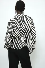 Camisa de manga larga con estampado de cebra, cuello solapa, escote en pico y cierre frontal con botones. Presenta un diseño con nudo en el bajo delantero y puños abotonados.