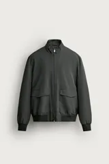 Cazadora regular fit de tejido técnico color gris oscuro, con cuello alzado, manga larga, bolsillos delanteros con solapa y cierre frontal de cremallera.
