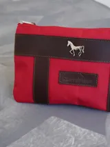 Sobre cartuchera de lona naranja con detalles en cuero marrón, cierre superior y aplique metálico de caballo en el frente.