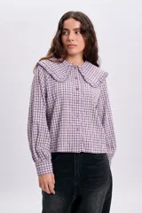 Camisa de manga larga con estampado a cuadros en tonos violeta y blanco, con cuello bobo grande con volados y cierre frontal de botones.