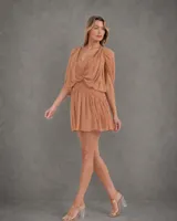 Vestido corto de gasa color durazno, con escote en V, drapeados en el frente y detalle de cadena dorada. Presenta mangas cortas tipo capa y cintura elástica con falda fluida.