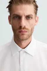 Camisa blanca de manga larga con cuello italiano y cierre frontal de botonadura. Corte regular fit.