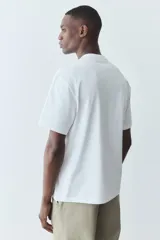 Remera blanca de corte holgado con cuello redondo ribeteado y hombros caídos. Confeccionada con tejido funcional COOLMAX®, una fibra de poliéster de secado rápido que elimina la humedad y regula la temperatura corporal.