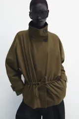 Parka amplia de Zara Woman Collection confeccionada en hilatura con mezcla de algodón, en color verde militar. Presenta cuello alto, manga larga con trabillas y botón, bolsillos laterales ocultos en costura, cintura ajustable con cordones y cierre frontal con botones.
