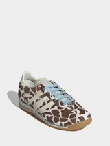 Championes Adidas modelo SL 72 OG con diseño de perfil bajo. Presentan una parte superior de piel con acabado de pelo de poni con estampado animal print de manchas marrones y blancas. Incluyen las icónicas tres tiras laterales en color crema, cordones celestes y suela de goma con entresuela de EVA.