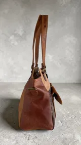 Cartera tipo tote de cuero en combinación de tonos marrones y beige, con diseño estructurado, doble asa de hombro, bolsillo frontal con solapa de pelo con estampado animal print, herrajes metálicos y llavero decorativo de la marca.